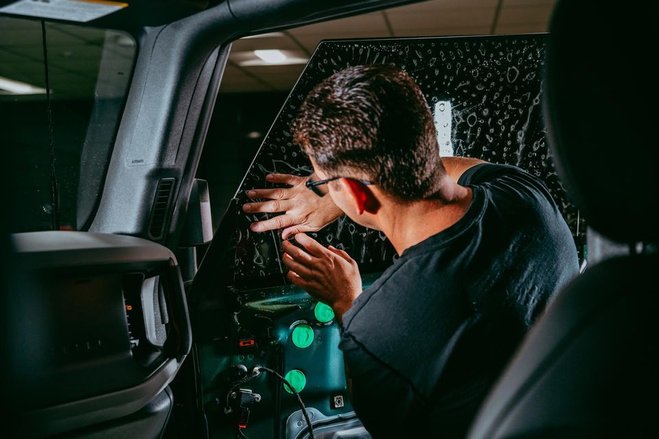 Person in a car shielding from shattered glass, with red blood on hand and window, near a green bottle.