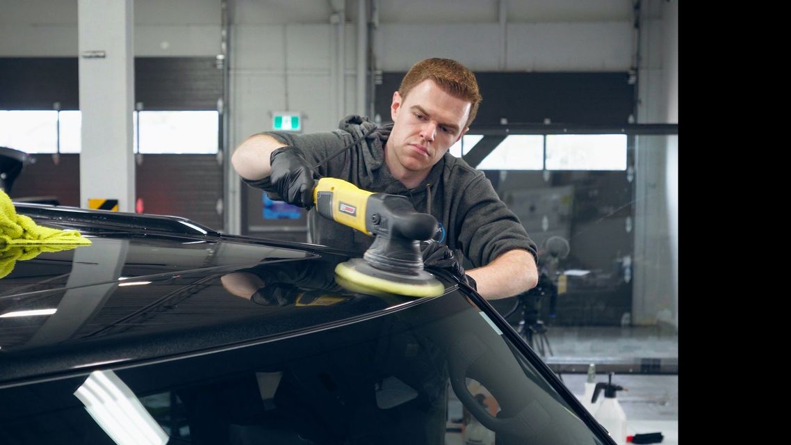 Technician polishing a black car in an auto detailing shop