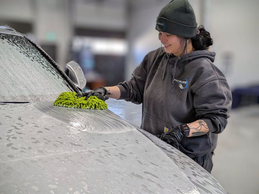 Person washing a gray car with a green sponge in a car wash.