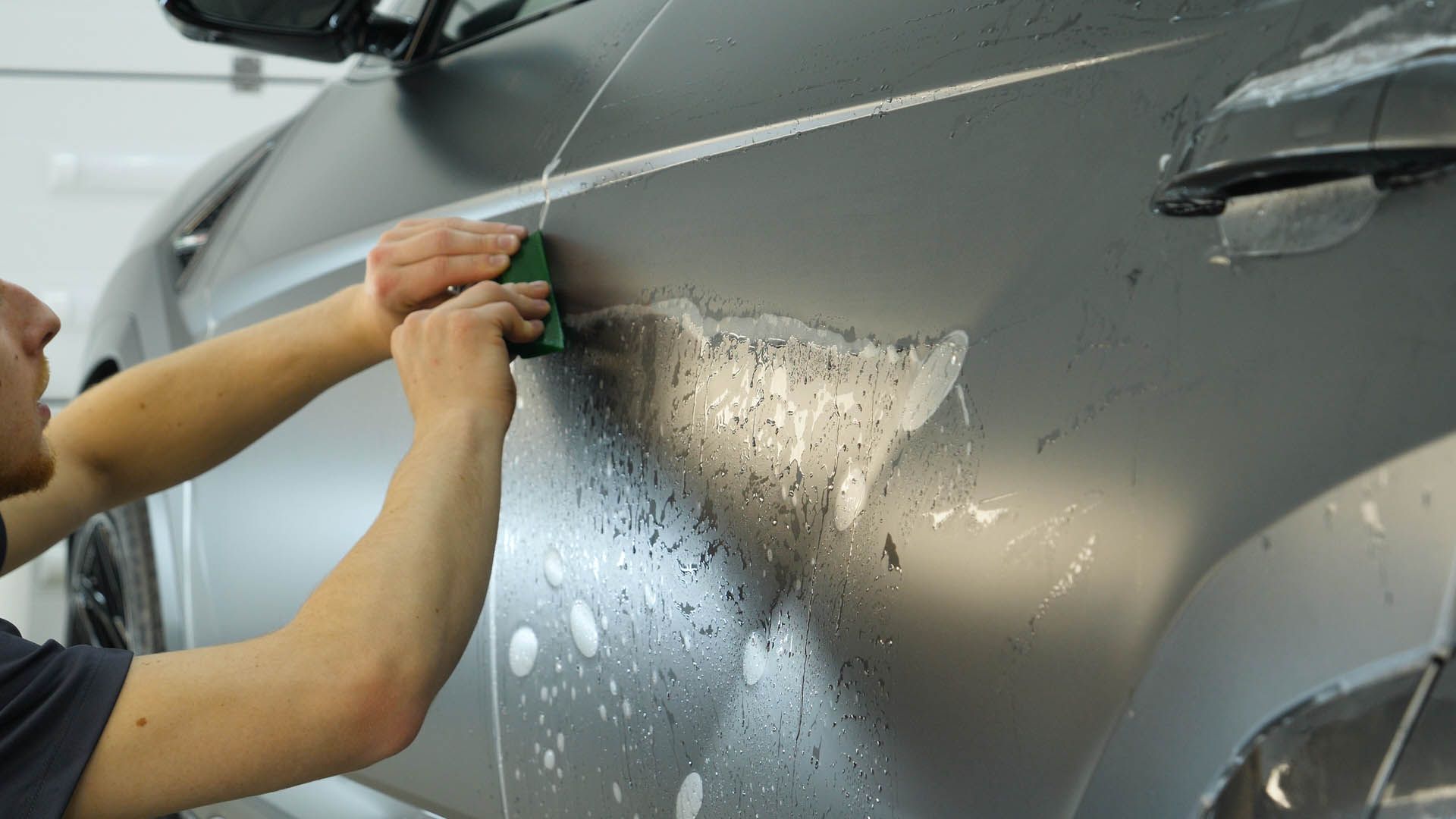 Person applying film to a gray car door with a squeegee in a workshop