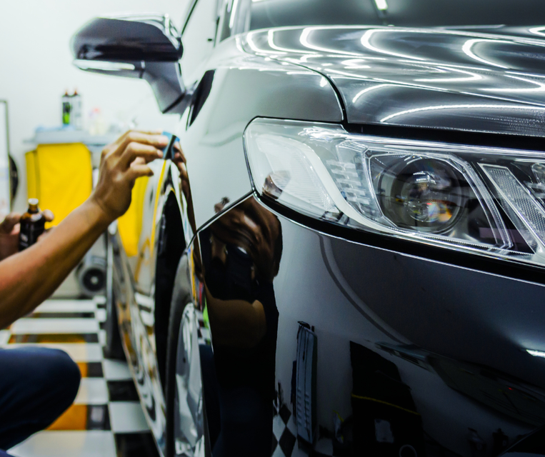 Technician polishing a black car in an auto detailing shop