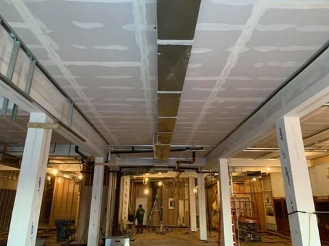 Renovation site with exposed ceiling panels, columns, and workers in a large unfinished interior.