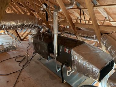Attic HVAC ductwork with insulated metal vents and furnace unit among wooden rafters