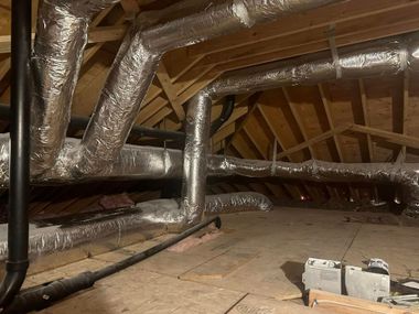 Attic with exposed ducts and insulation under a wooden roof, with a small ladder on the floor.