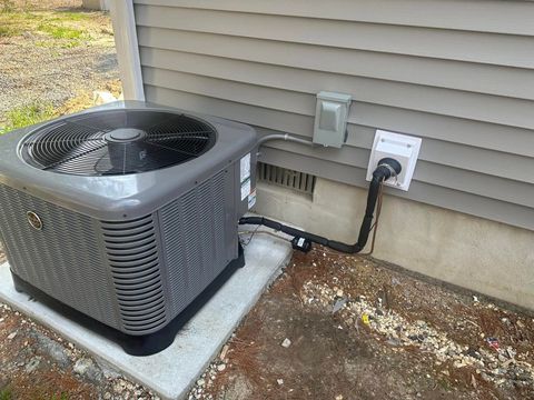 Outdoor air conditioner unit beside a house wall, with conduit and electrical outlet connection