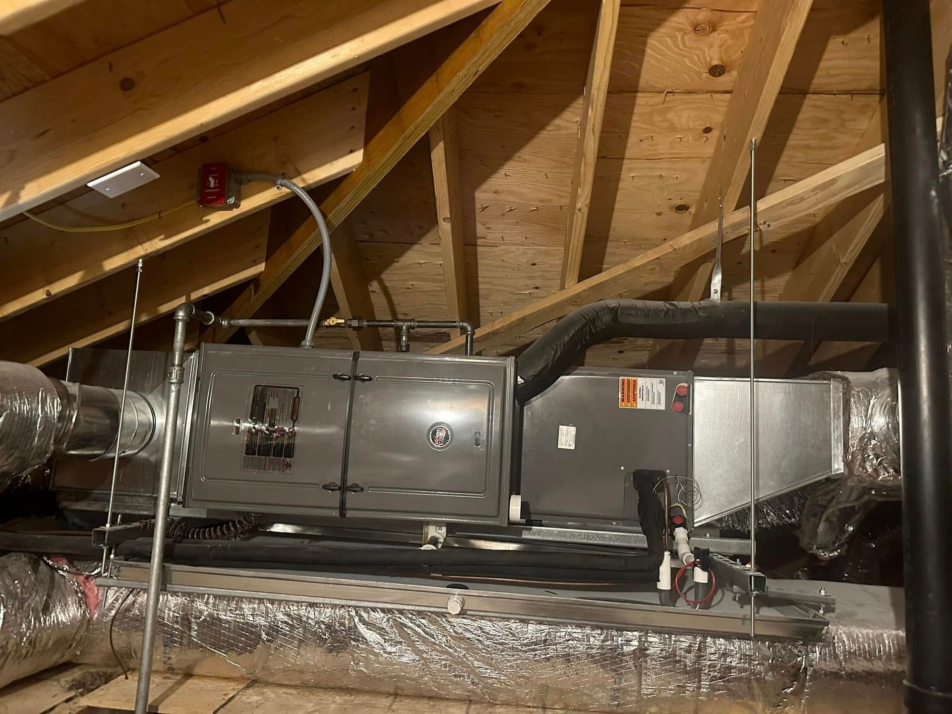 HVAC ductwork and insulation in an attic with exposed wooden rafters