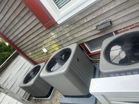 Three outdoor air conditioning units beside a house with gray siding and red trim.