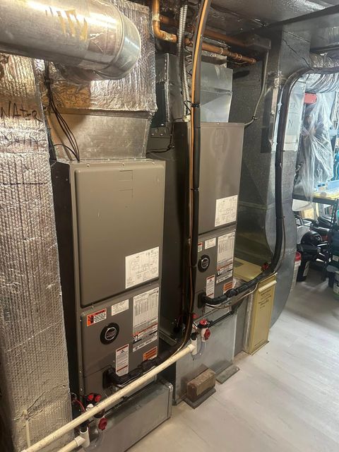 Basement utility room with two gray HVAC units, ductwork, and exposed piping along a wall