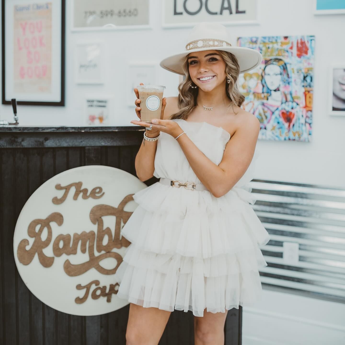 A woman in a white dress is standing in front of a sign that says the ramblin tap.