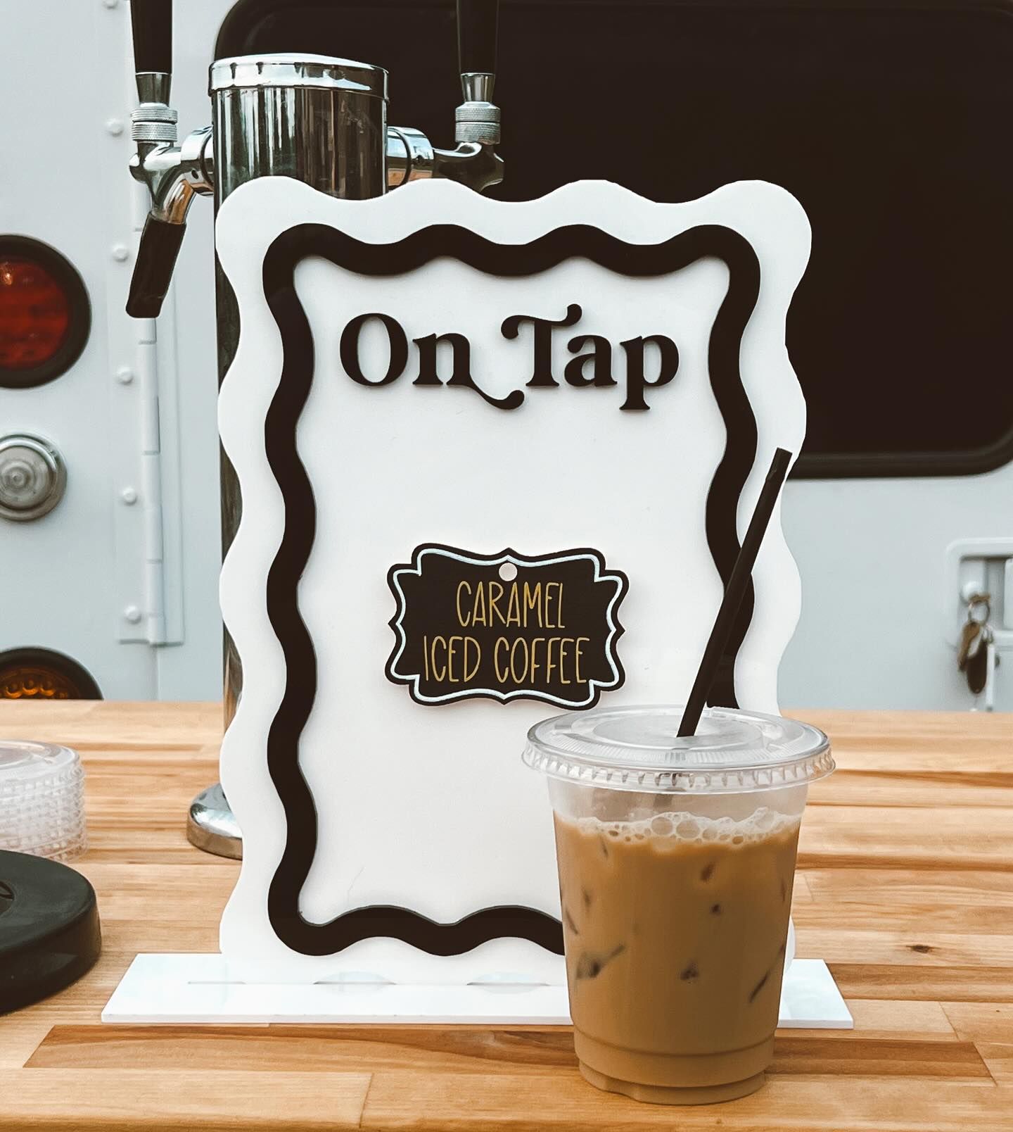 A cup of caramel iced coffee next to a sign that says on tap