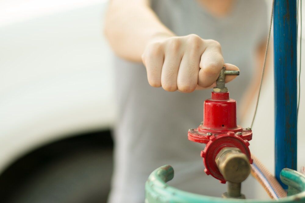 A hand is reaching out to turn on a gas canister. 