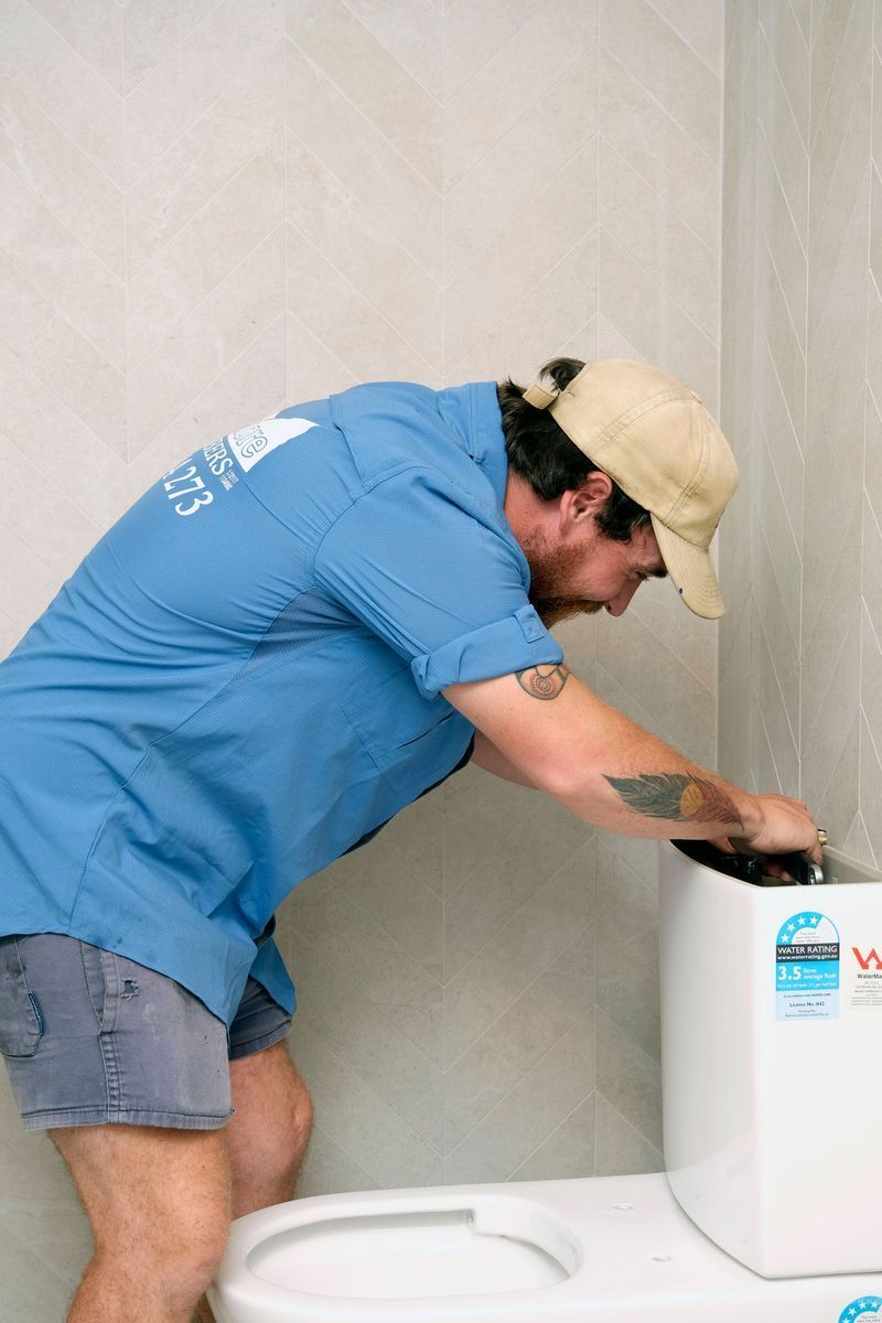 A Man in a Blue Shirt is Working on a Toilet — Foreshore Plumbers in Tuncurry, NSW