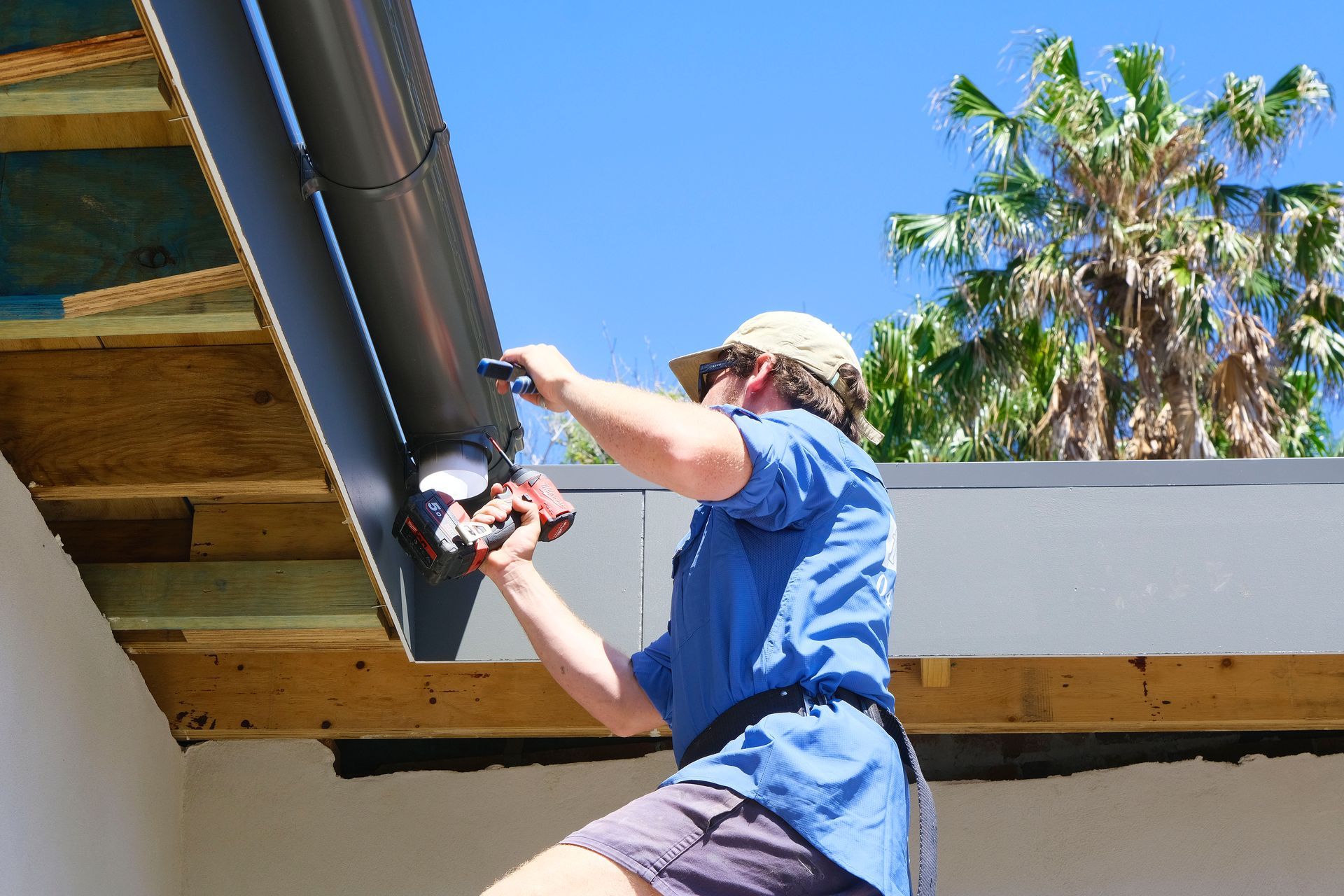 A Man is Working on a Gutter on the Roof of a House — Foreshore Plumbers In Tuncurry, NSW