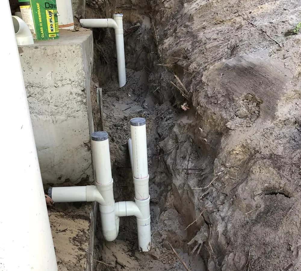A Bunch of White Pipes Are Laying in the Dirt — Foreshore Plumbers In Tuncurry, NSW