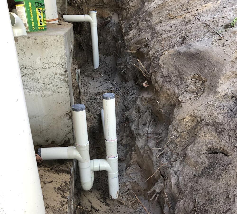 A Bunch of White Pipes Are Laying in the Dirt — Foreshore Plumbers In Tuncurry, NSW