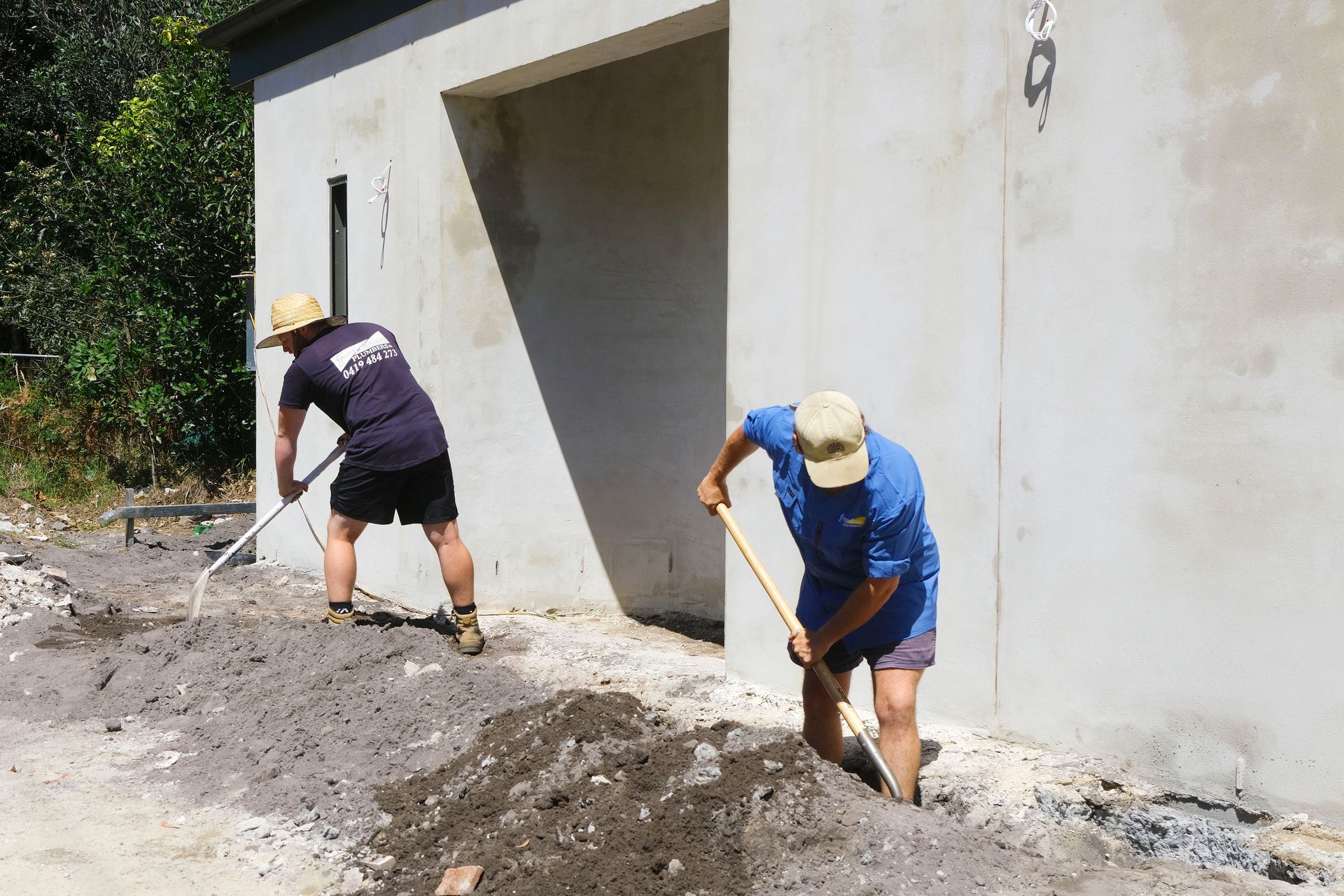Two Men Are Digging in the Dirt in Front of a Building — Foreshore Plumbers In Tuncurry, NSW