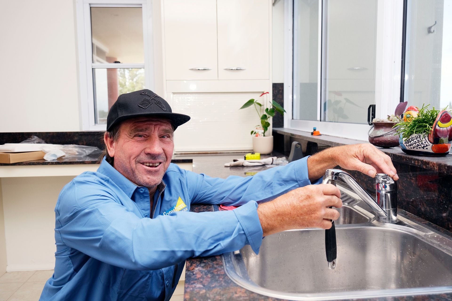 A Man is Fixing a Faucet in a Kitchen — Foreshore Plumbers In Nabiac, NSW