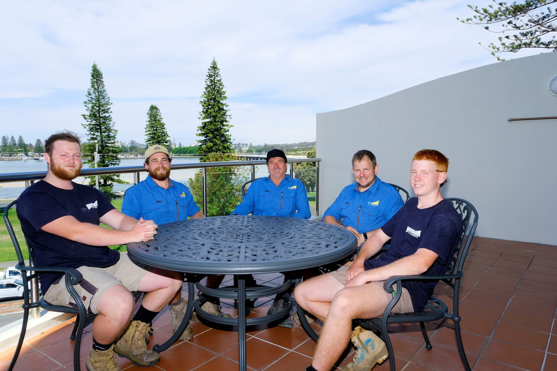 A Group of Men Are Sitting Around a Table on a Balcony — Foreshore Plumbers In Tuncurry, NSW