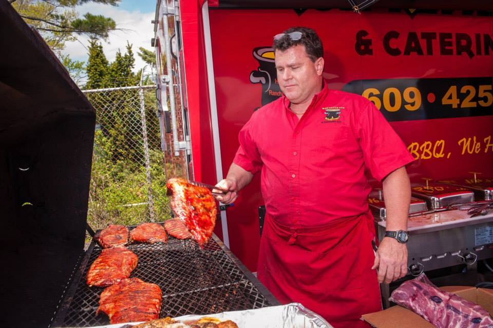 A man in a red apron is cooking meat on a grill in front of a sign that says 609 425