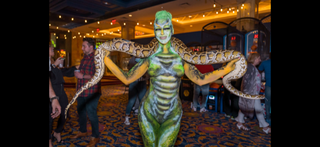 A woman with her body painted like a snake is holding a snake.