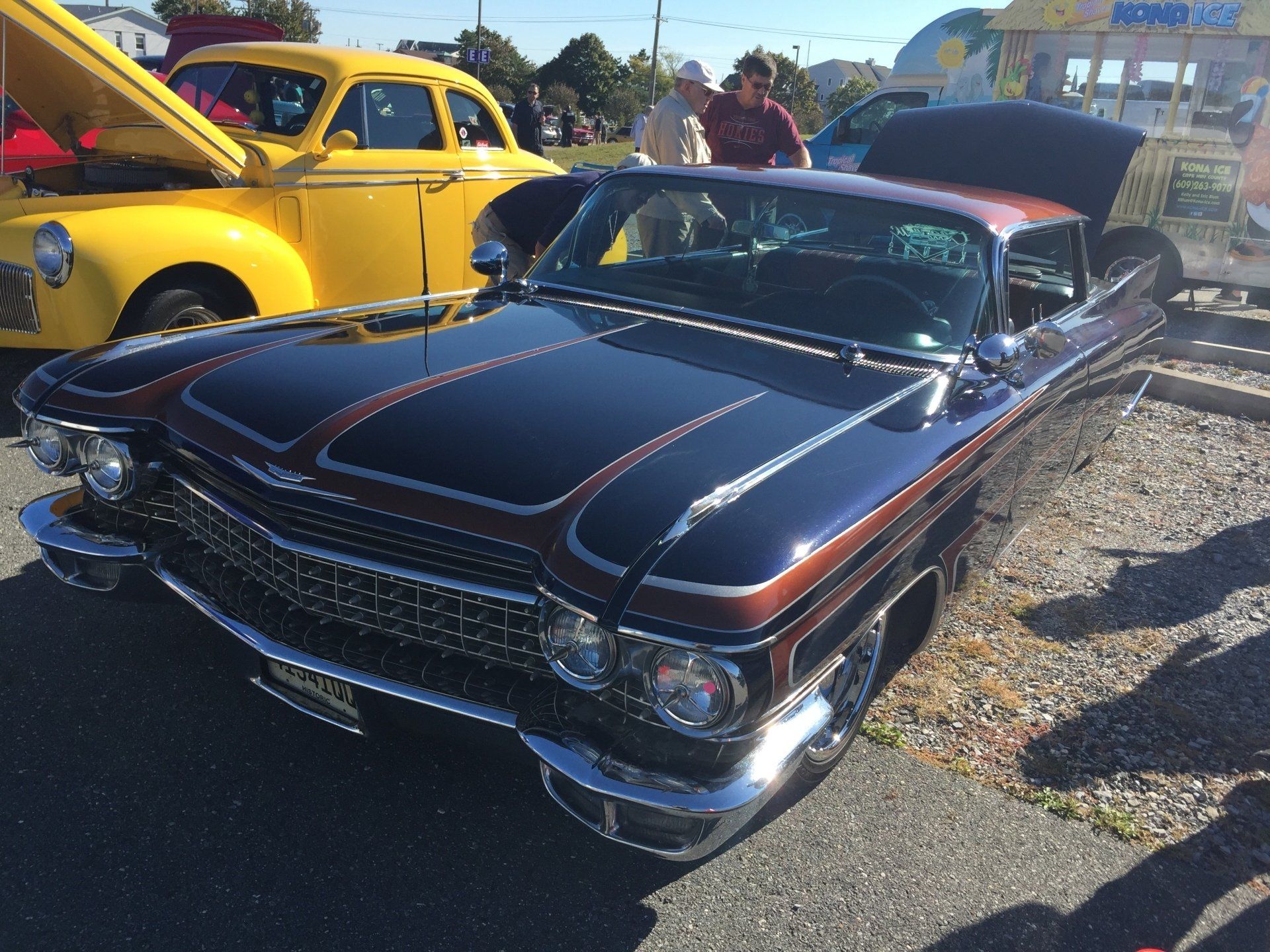 A black car with the hood up is parked next to a yellow car