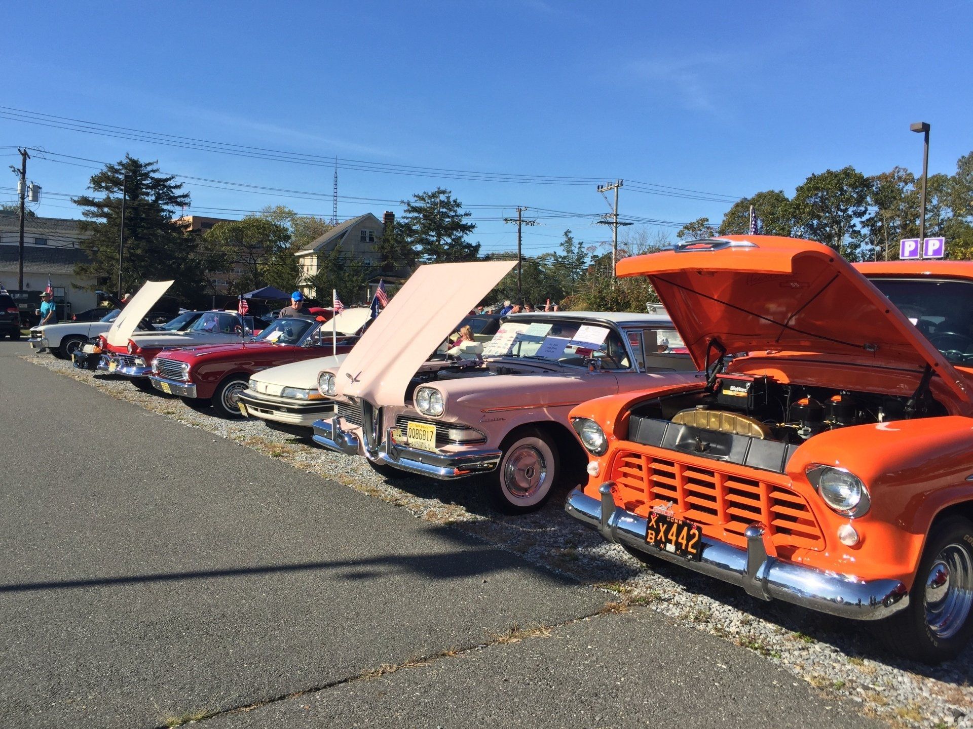A row of old cars are parked in a parking lot with their hoods open.