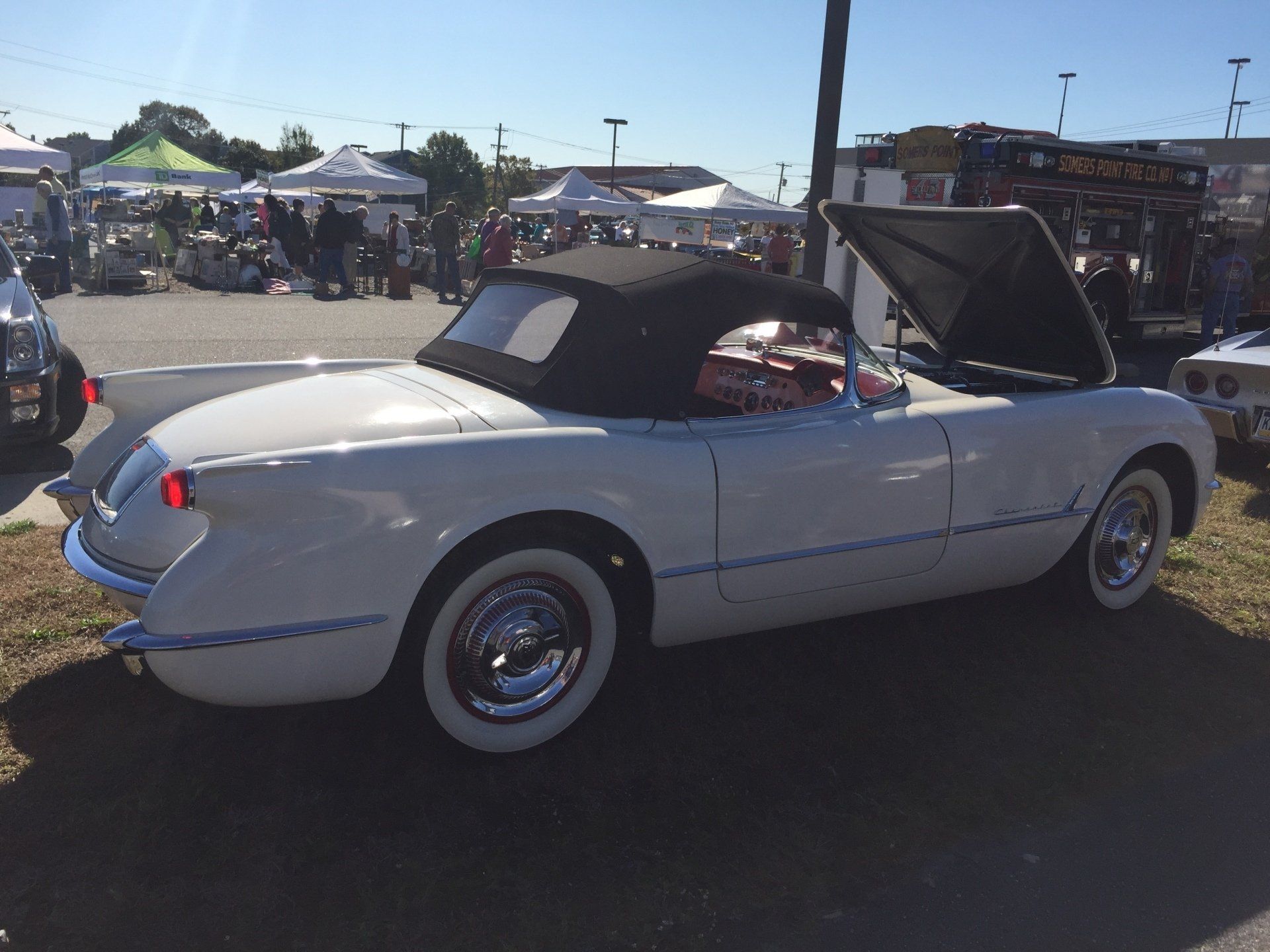 A white convertible with the hood up is parked in a parking lot