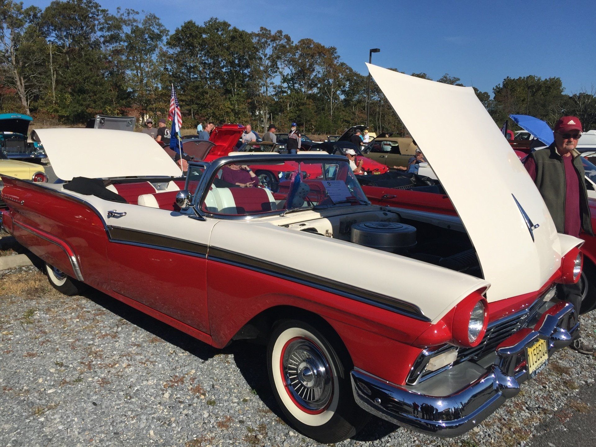 A red and white car with the hood up is parked in a gravel lot.