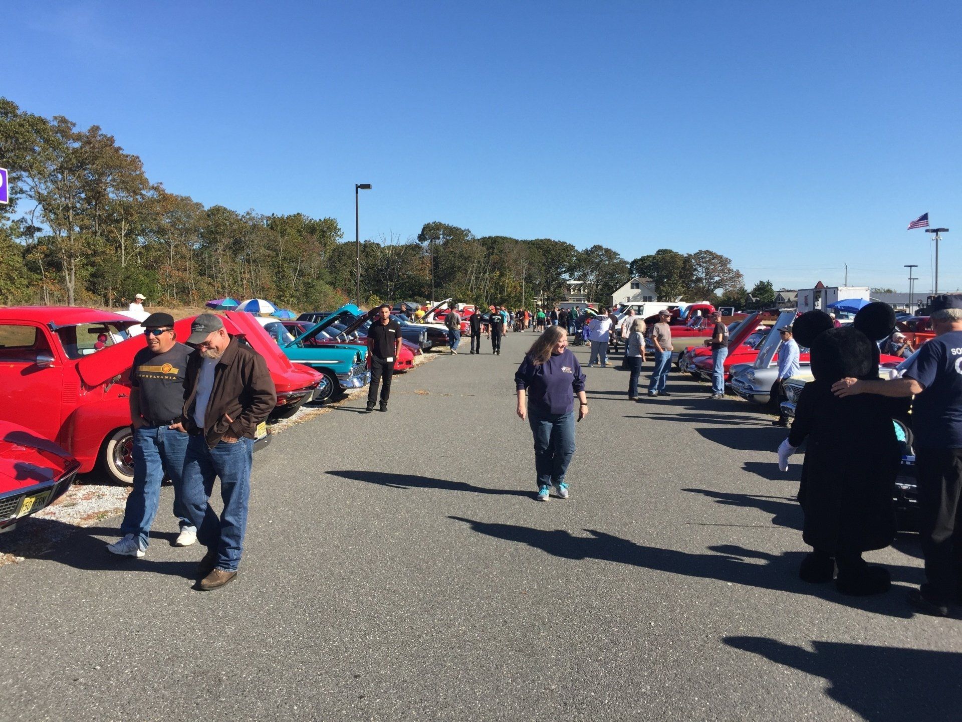 A group of people are standing in a parking lot looking at cars.