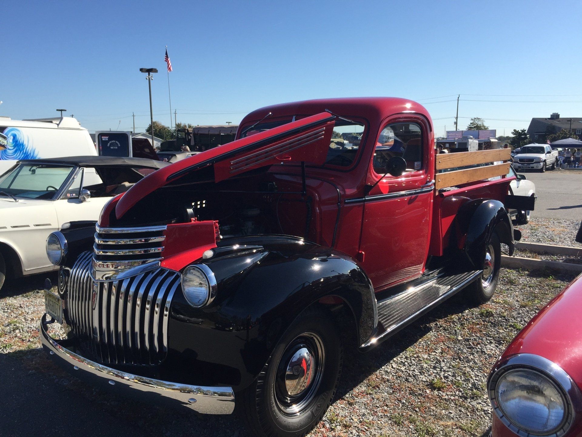 A red truck with the hood up is parked in a gravel lot