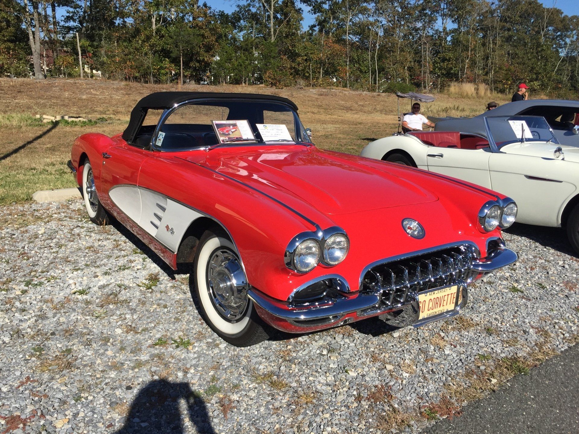 A red corvette convertible is parked in a gravel lot.