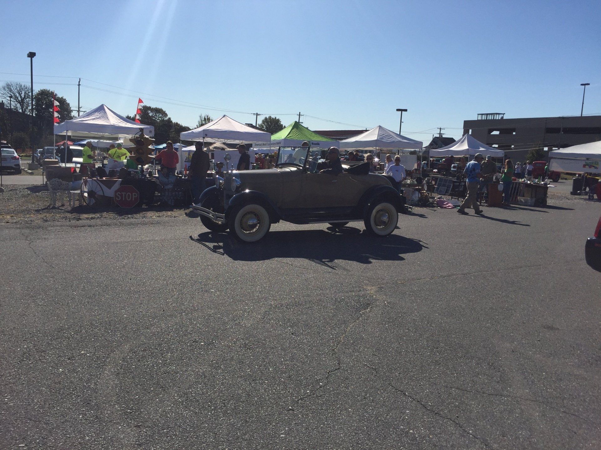 An old car is parked in a parking lot surrounded by tents