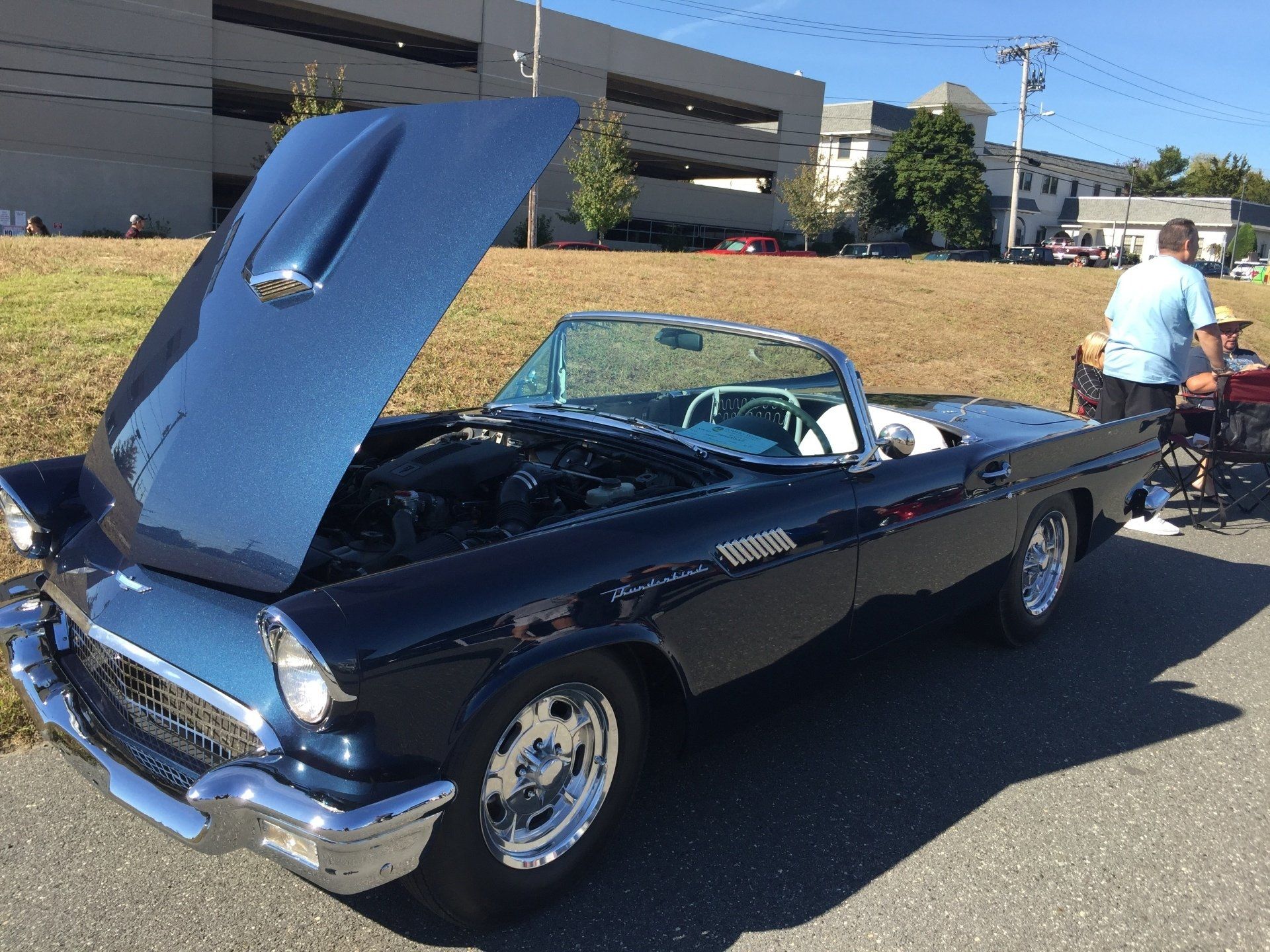 A blue car with the hood up is parked on the side of the road