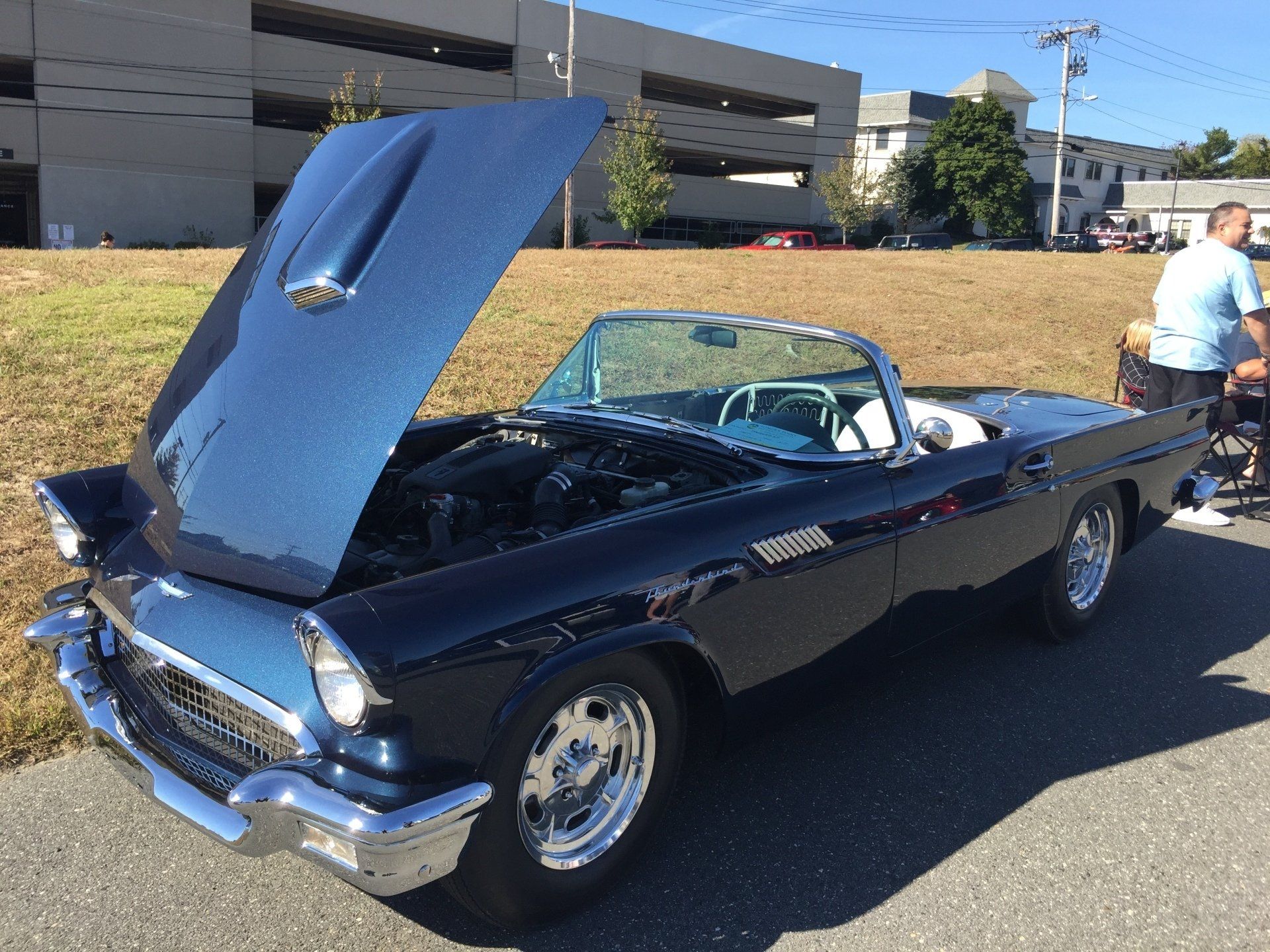 A blue car with the hood up is parked on the side of the road