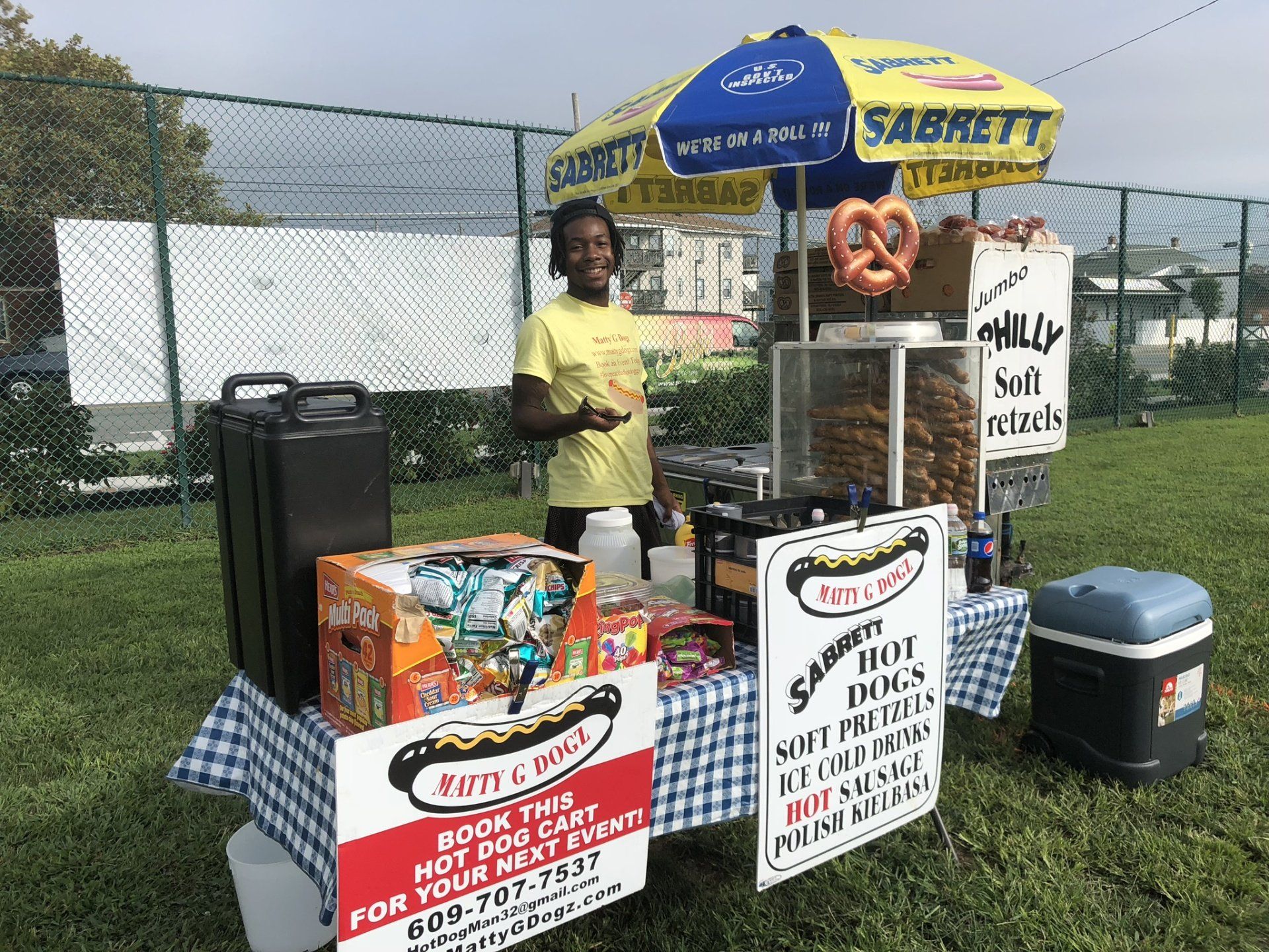 A man is standing in front of a hot dog stand.