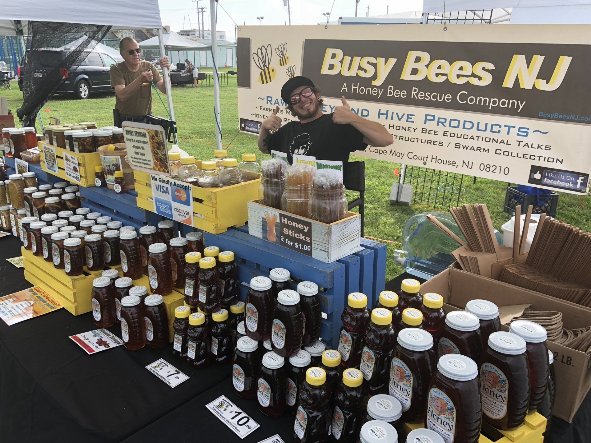 A man is standing in front of a table filled with bottles of honey.