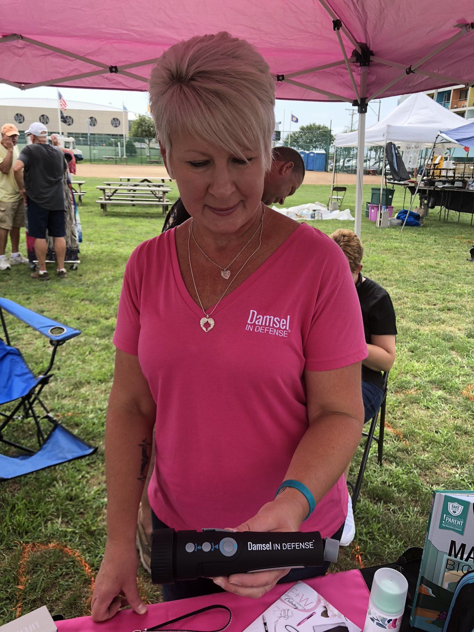 A woman in a pink shirt is standing under a pink tent holding a device.