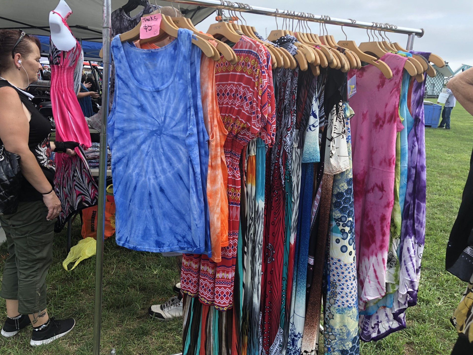 A woman is looking at clothes hanging on a rack at a market.