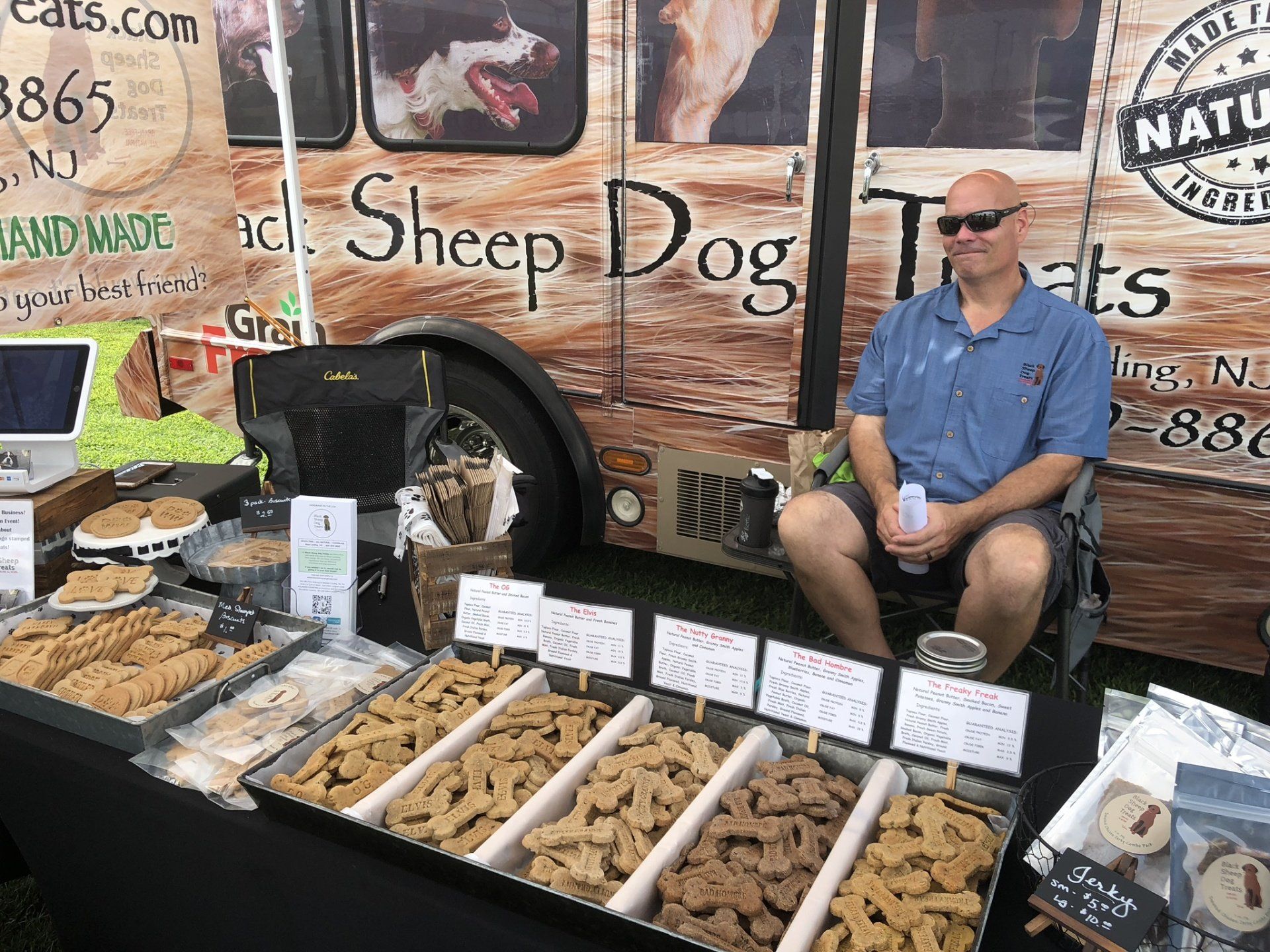 A man is sitting in front of a truck selling dog treats.