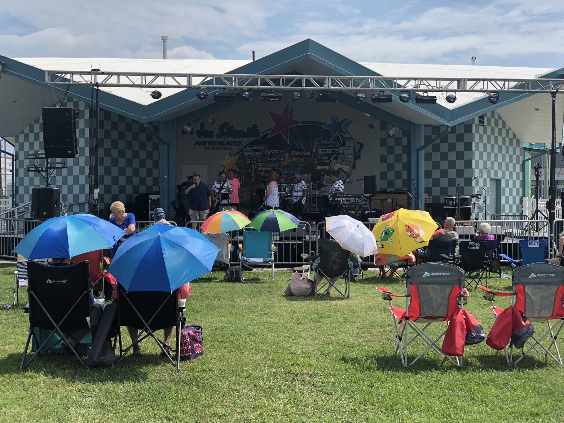 A group of people sitting in chairs with umbrellas in front of a stage.