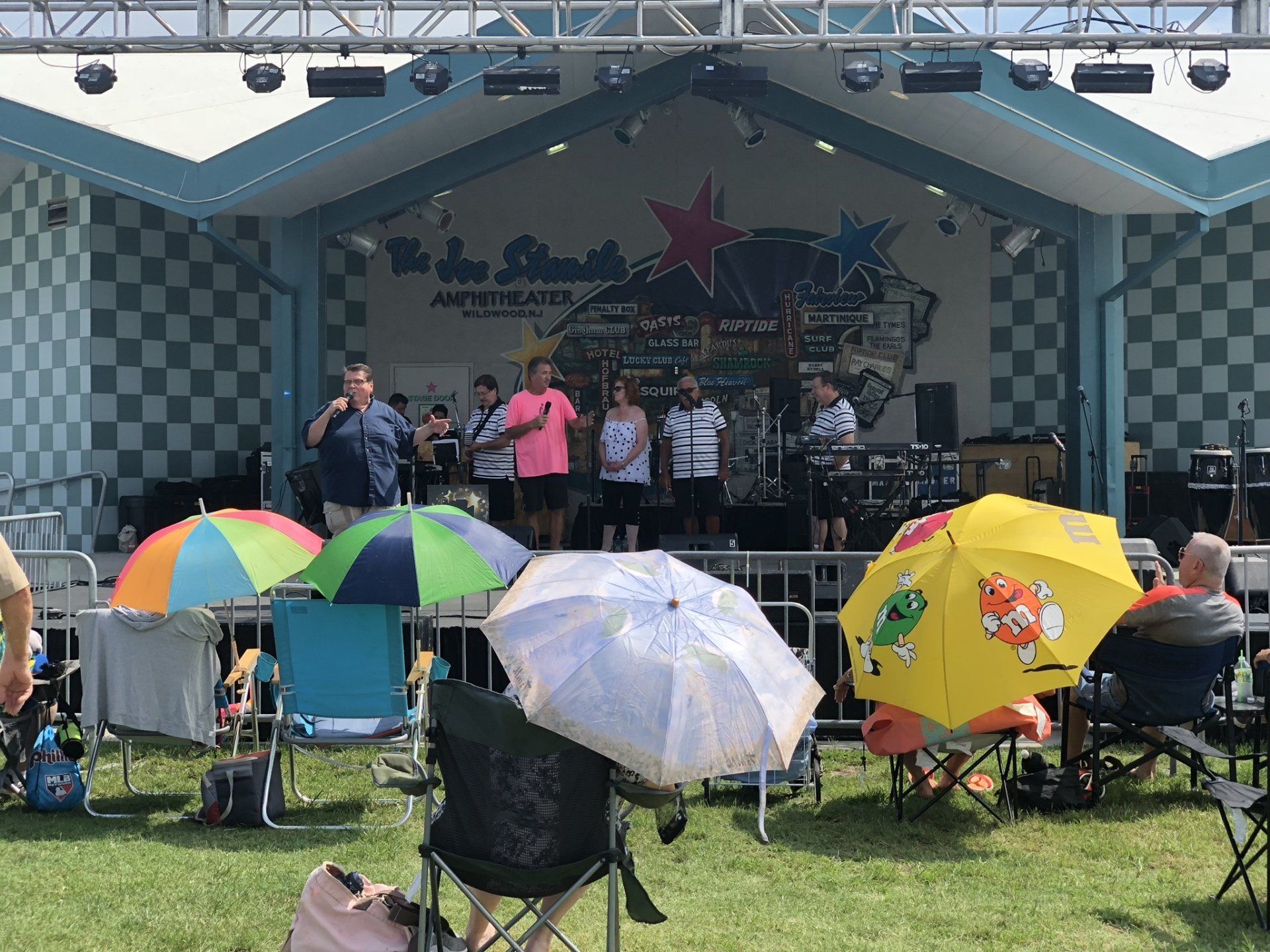 A group of people sitting in chairs with umbrellas in front of a stage.