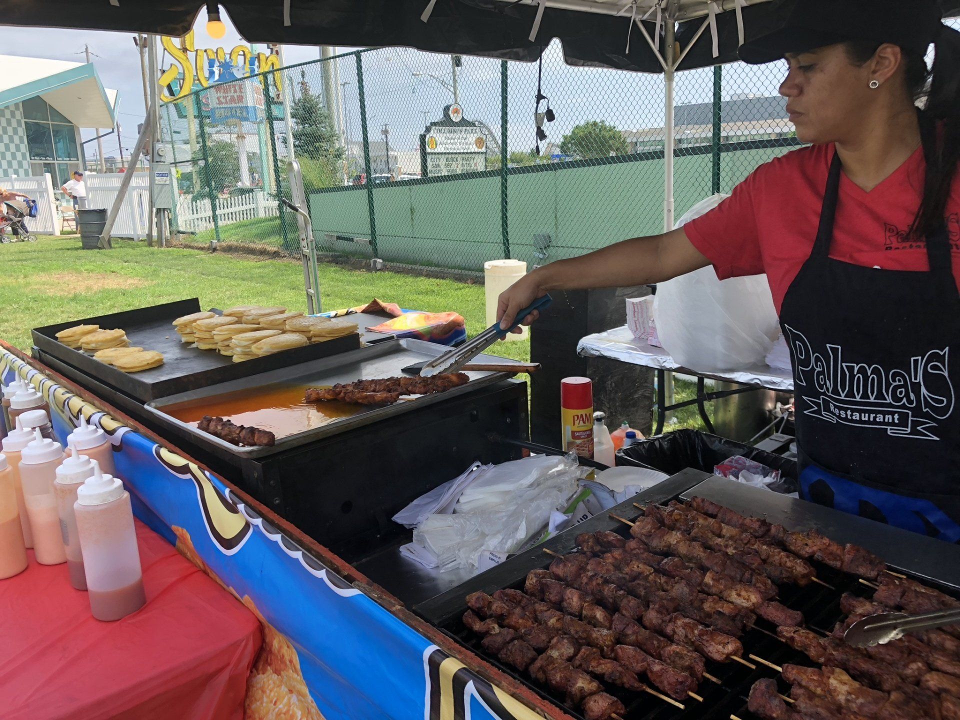 A woman is cooking food on a grill under a tent.