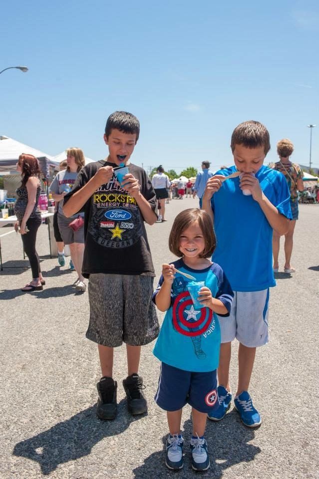 Three children are standing on the side of the road eating ice cream.