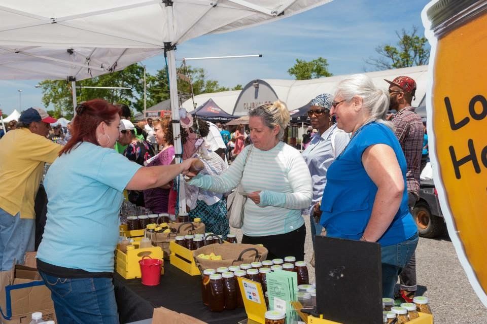 A group of people are standing around a table with jars of honey.