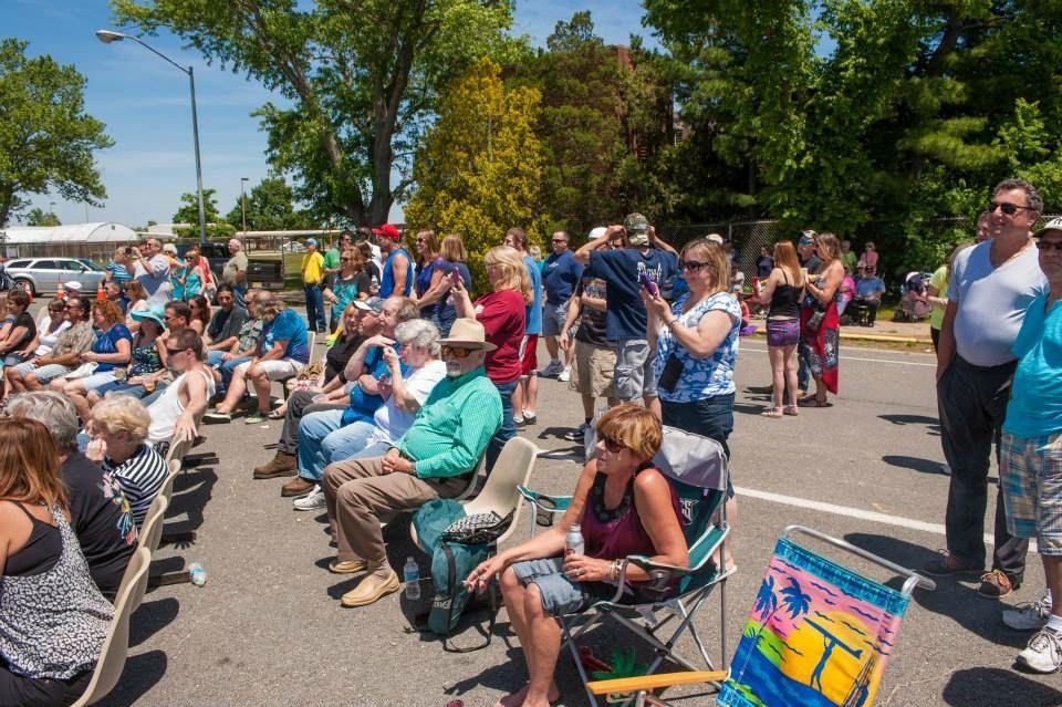 A group of people are sitting in a parking lot watching a parade.