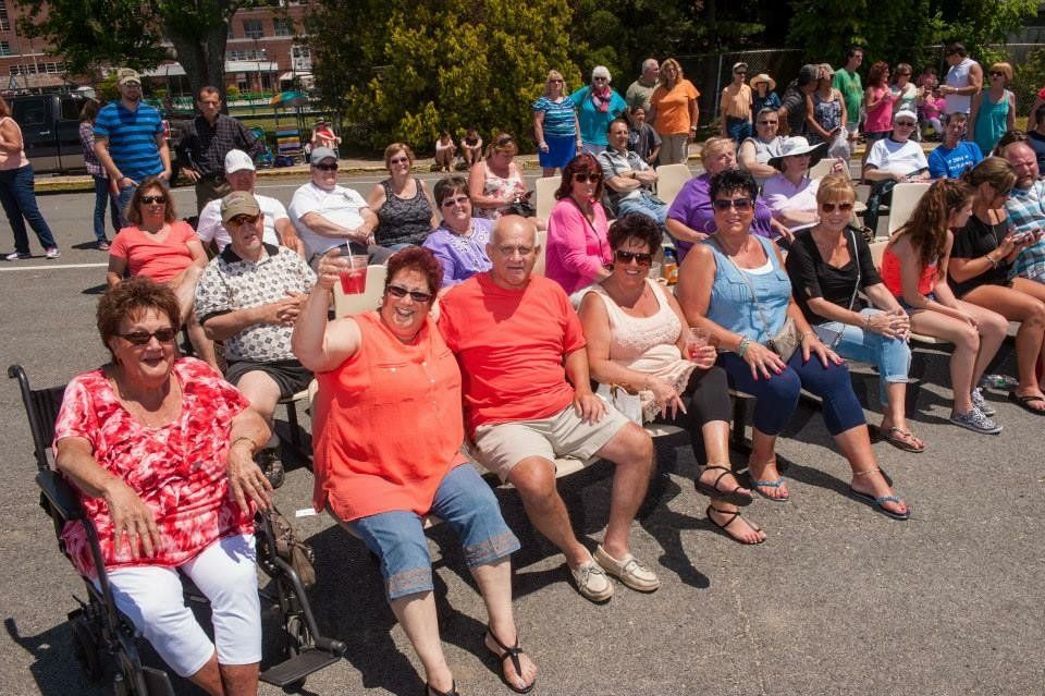 A group of people are sitting on a bench in a parking lot.