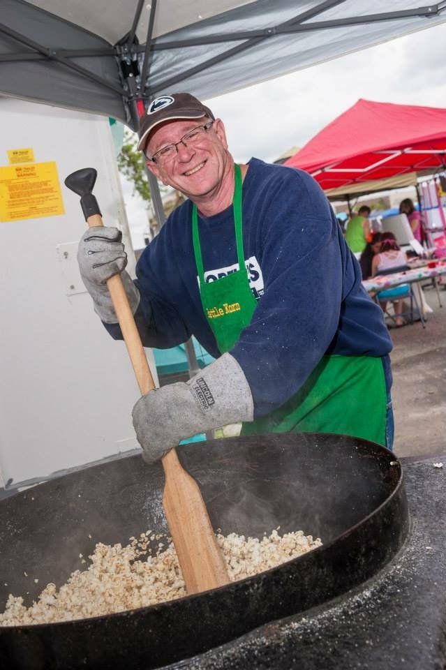 A man is stirring food in a large pot with a wooden spoon.