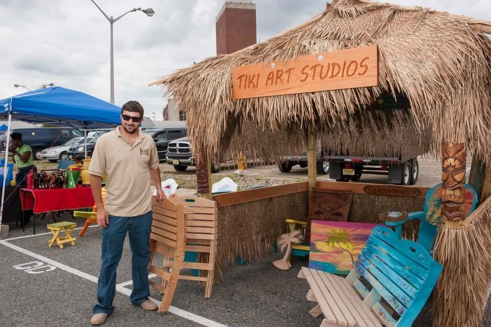 A man stands in front of a tiki art studios sign