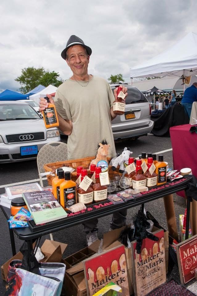 A man is standing in front of a table holding a bottle of hot sauce.