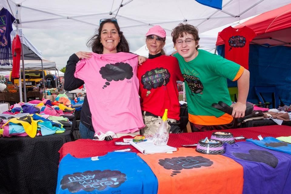 A group of people standing around a table with shirts on it.